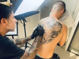 Instructor Mr. White tatuando la espalda de un alumno durante el Curso de Tatuaje Homologado en Tattoo School Madris