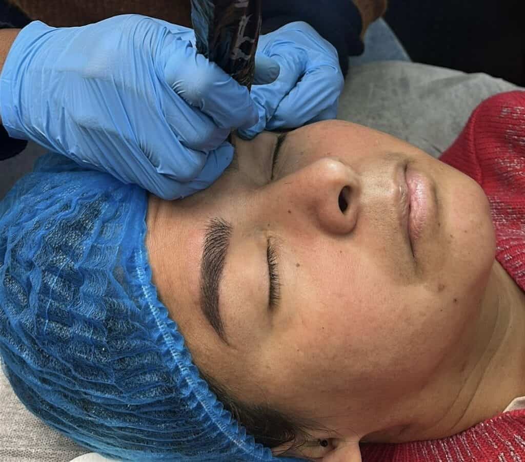 Tatuaje facial en proceso, técnica de tatuaje en piel de una mujer dormida con gorro azul.