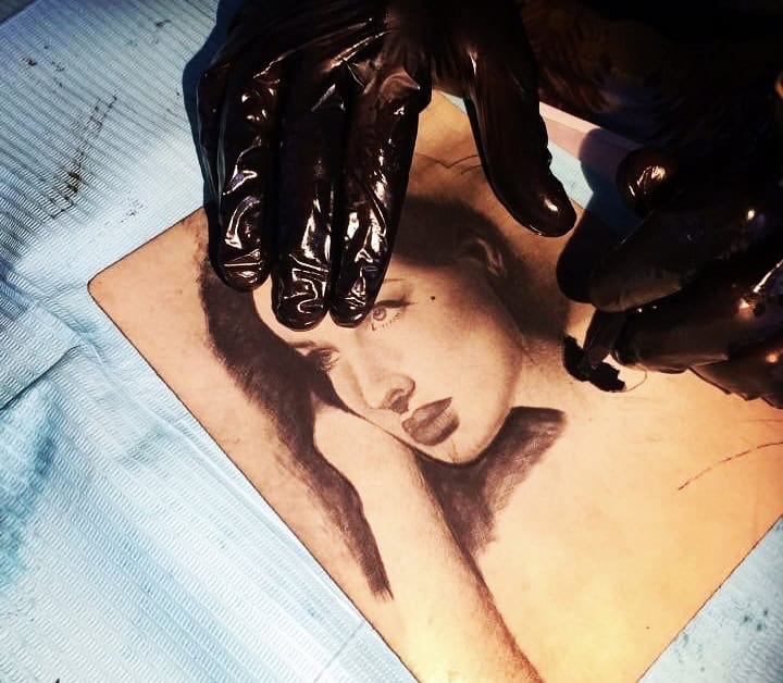 Tatuaje de retrato en piel con detalles realistas y sombreado en tonos oscuros.