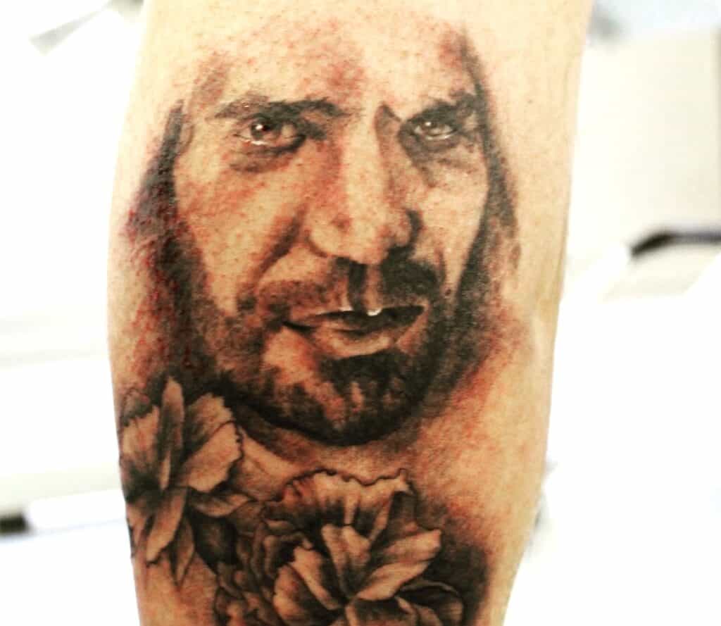 Retrato de un hombre en estilo realista, tatuado en el brazo con detalles finos y sombreado.