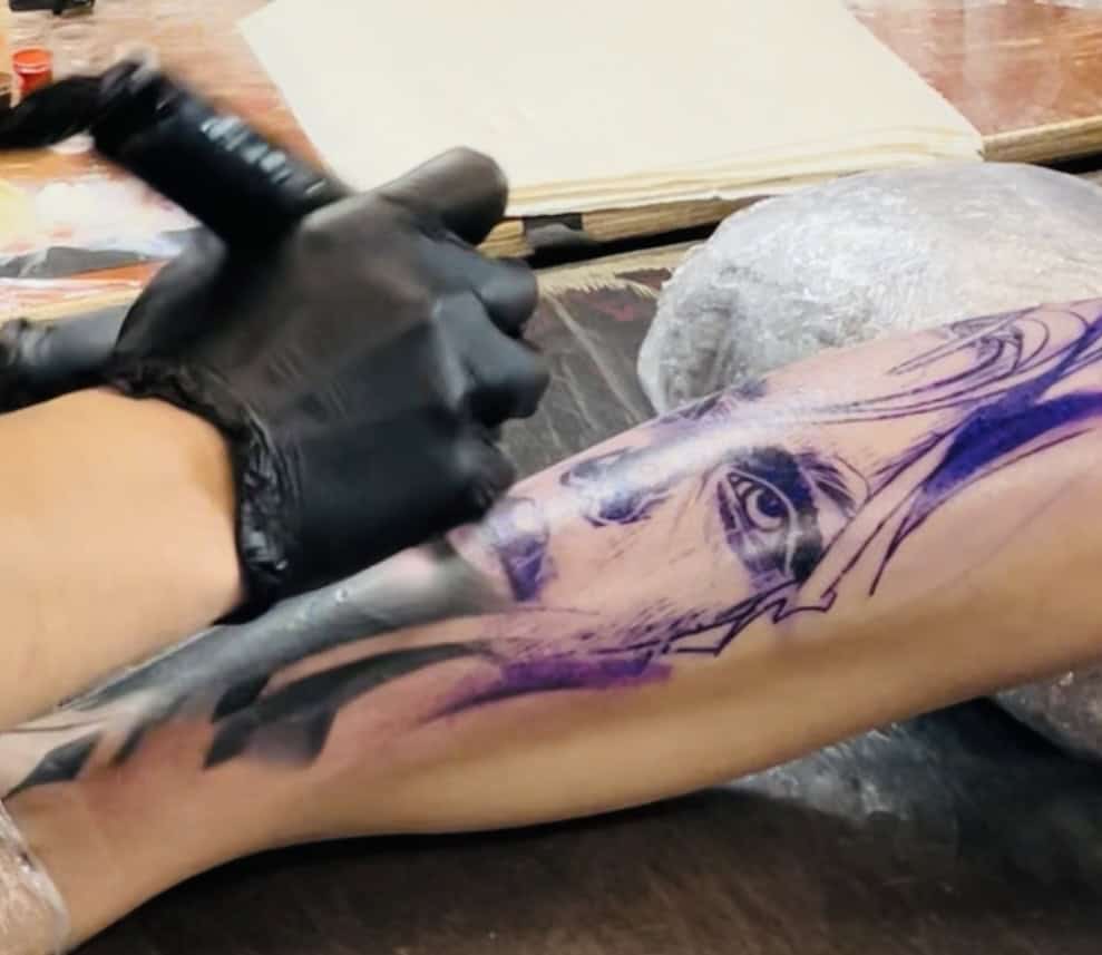 Tatuaje en proceso en el brazo con un artista en acción, usando guantes y tinta.